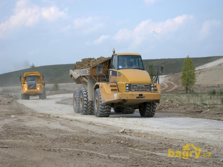 Kloubový dempr Caterpillar 735, za ním Volvo A35E