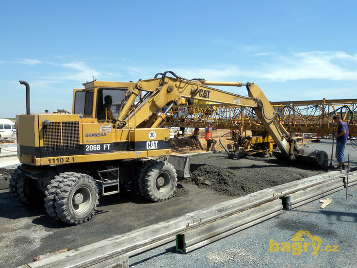Kolové rypadlo Caterpillar 206B FT firmy Skanska DS rozhrnuje beton před finišerem