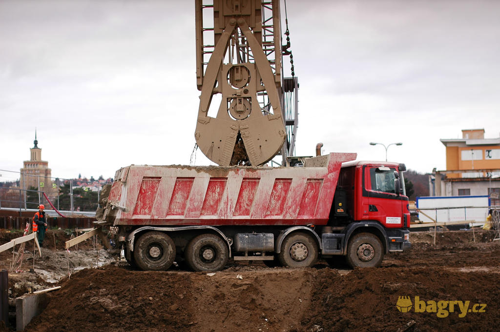 Drapáková souprava Bauer MC 64 pro těžbu podzemních stěn vysýpá zeminu na sklápěč Scania 124c 470 firmy Zakládání staveb